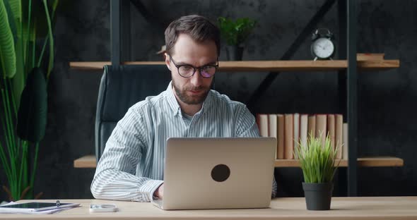 Concentrated Man Freelancer in Eyeglasses Working at Laptop at Modern Workplace Remotely at Home