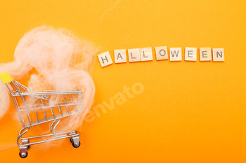 shopping cart with spider web and the inscription halloween on orange background.