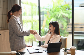 Cheerful businesswomen shaking hands in the office. Business etiquette, teamwork and trust