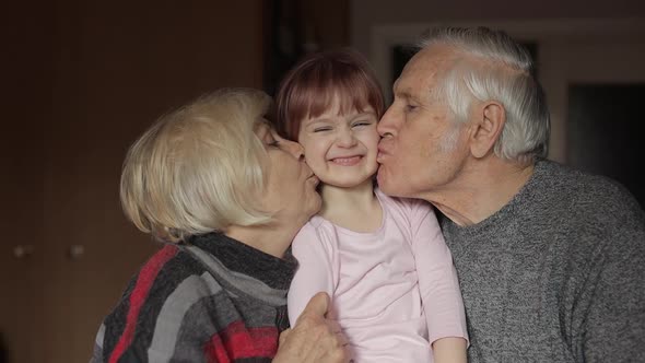 Grandfather and Grandmother Kissing on Cheeks Their Kid Granddaughter at Home