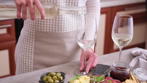 Woman Pouring Wine to a Glass From a Bottle at Domestic Kitchen with Meat and Cheese Plater on the