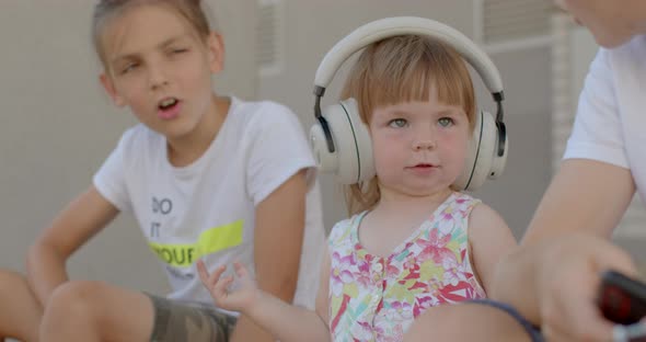 Portrait of Little Cute Girl in Headphones with Brothers in Yard