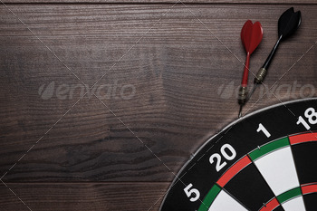 Target And Two Darts Over Brown Wooden Table Background