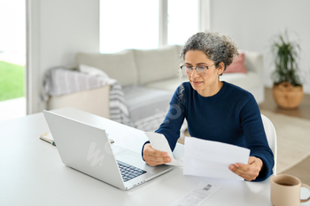 Mature lady paying bills online checking medical receipts bills using laptop.