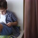 Cute little boy uses a white tablet PC on a windowsill at home - VideoHive Item for Sale