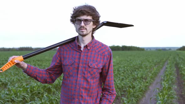 The farmer holds a shovel in his hand on an agricultural field, harvest time.