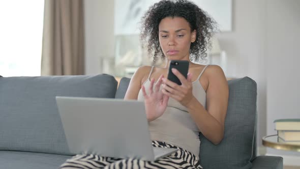 African Woman Using Smartphone and Laptop at Home