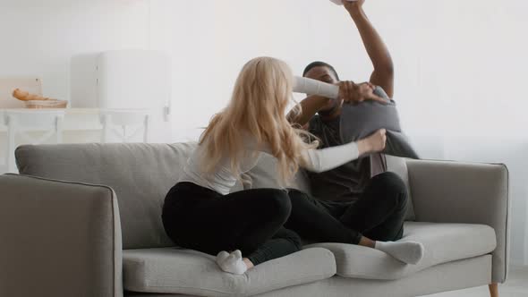 Happy Diverse Couple Having Pillow Fight On Sofa At Home