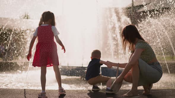 Playful Little Children with Mother Have Fun Near Fountain