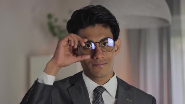 Indian businessman adjusts glasses and nods smiling behind camera, static