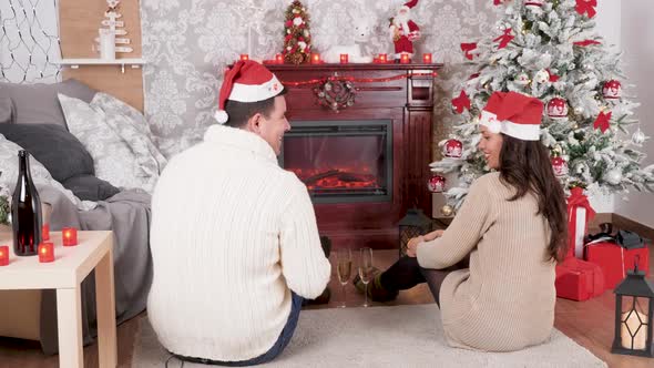 Inlove Couple Sitting on the Floor in Front of a Fireplace in Christmas Decorated Room