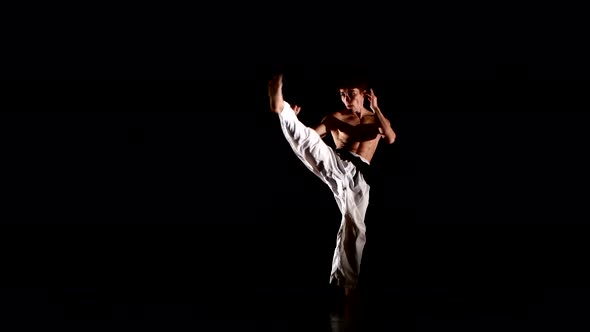 Young Karate or Taekwondo Man Jumping, High Kick and Fist Punch Isolated on Black