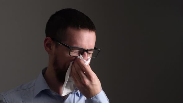 Young sick man with glasses sneezes into a tissue paper - Slow Motion