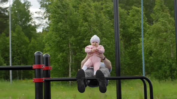 Fit Caucasian Dad Holding Baby Daughter and Doing Sit-Ups at Outdoor Gym