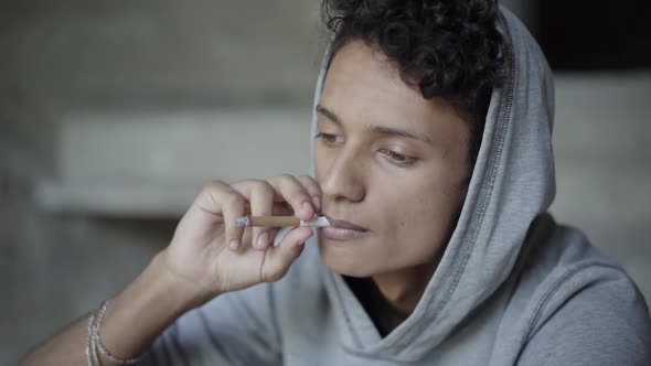 Close-up Portrait of Mixed-race Teenager Smoking Cigarette. Thoughtful Relaxed Teenage Boy in Hood