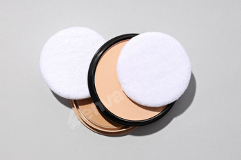 Face powder, with a puff for application, on a light background.