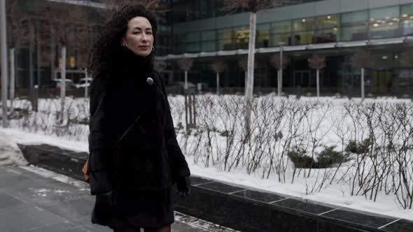 A Curlyhaired Woman in a Fur Coat Walks Around the Winter City Enjoying a Beautiful Day