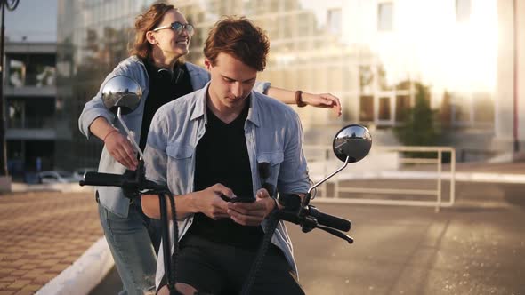 Young Caucasian Man is Sitting on Bike and Scrolling His Mobile Phone