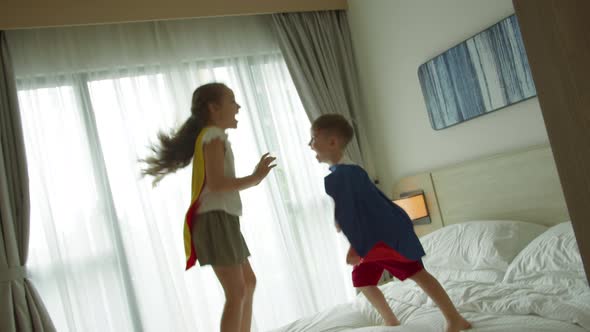 Children Playing Superheroes are Jumping in Room on Bedin Children's Room Two Children in Red and