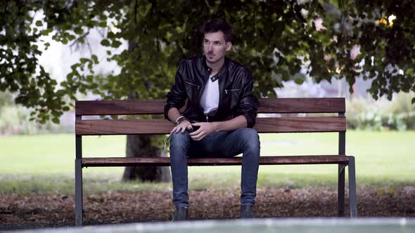 A young man in jeans, white T-shirt and a black jacket, wearing a green Covid-19 facemask, sitting o