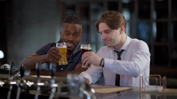 Two Happy Joyful Relaxed Men Clinking Beer Glasses Smiling Toasting Looking at Camera
