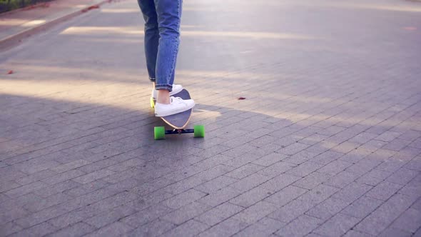 Closeup View of Woman's Legs in Blue Jeans and White Sneakers Skateboarding in the Cobblestone Road