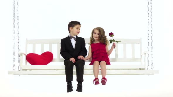Little Boy and a Little Girl Are Sitting on a Swing, Cute Chat. White Background. Slow Motion