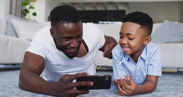 African american father and son wearing earphones and using smartphone together