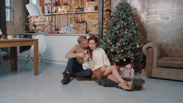 Couple in Love Sitting and Hugging Near the Christmas Tree While Drinking Champagne