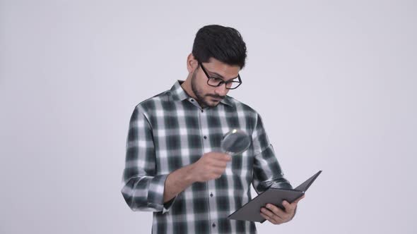 Young Handsome Bearded Indian Man Reading Book with Magnifying Glass