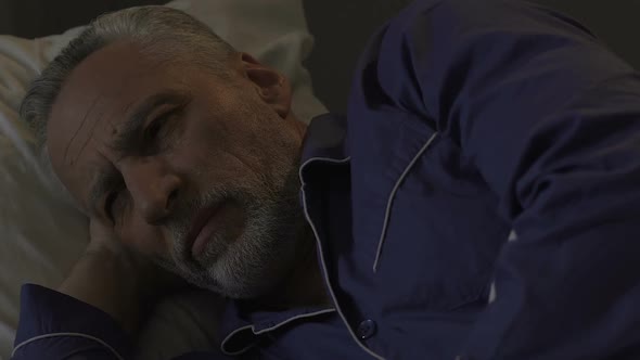 Bearded old male lying in bed awake unable to fall asleep at night sleeplessness