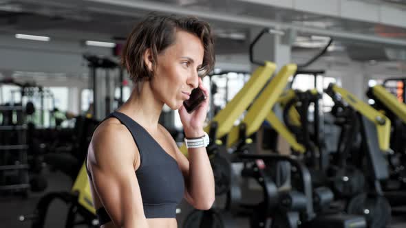 Mature Woman Is Making Biceps Exercise with Dumbbells in Gym and Speaking Phone.