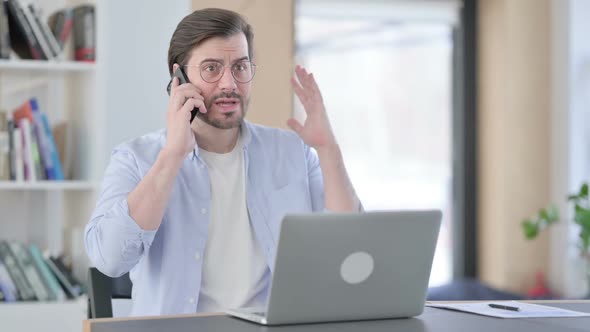 Angry Businessman with Laptop Talking on Smartphone