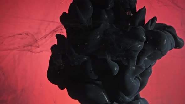 Black nacreous paint in water against red background.