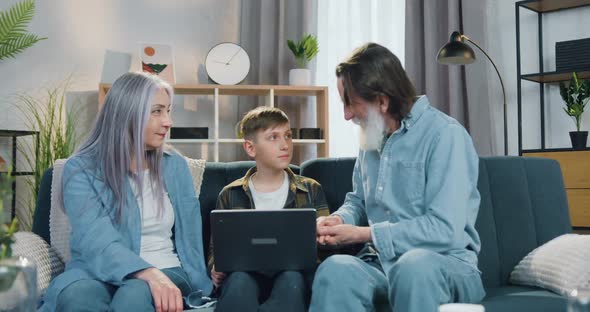 Grandparent Sitting on the Couch with their Teen Grandson which Studying Between them on Laptop