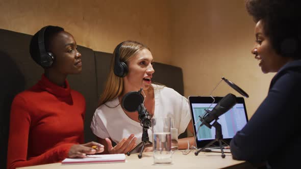 Three diverse female radio hosts wearing headphones talking on microphone for radio podcast