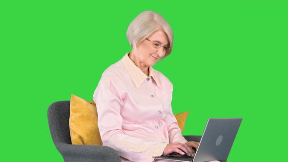 Attractive Senior Woman Surfing the Internet Sitting in a Comfortable Armchair on a Green Screen