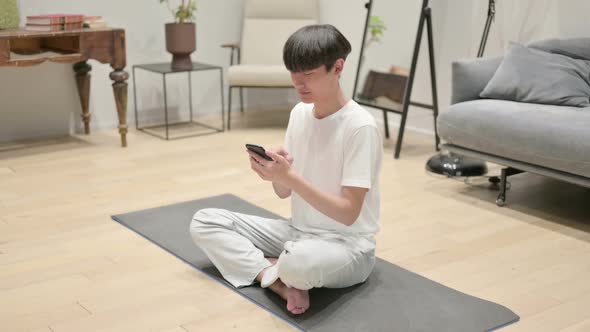 Asian Man Using Smartphone on Yoga Mat at Home