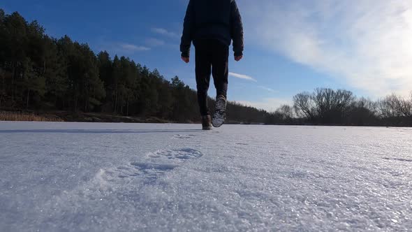 A man walks forward on the snow on the lake. Shoes close up