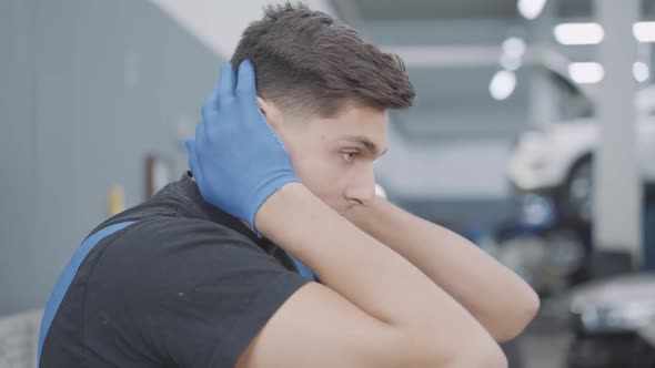 Closeup Side View of Stressed Young Auto Mechanic Holding Head in Hands and Sighing