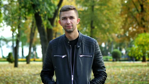 Portrait of Man Wearing Black Leather Jacket Walk in the Autumn Park, Looking at Camera