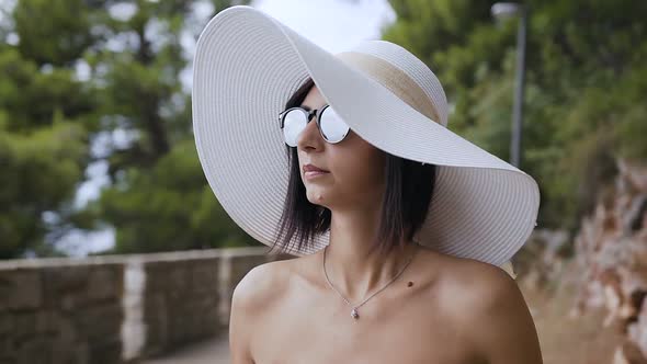 A Beautiful Brunette in a White Hat and Sunglasses Walks in the Park
