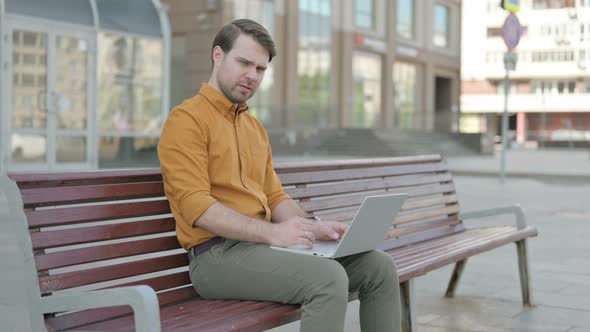 Thumbs Down by Young Man with Laptop Sitting on Bench