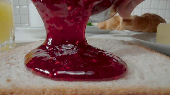 A Stream of Raspberry Jam Flowing From a Jar Onto Piece of Bread Toast