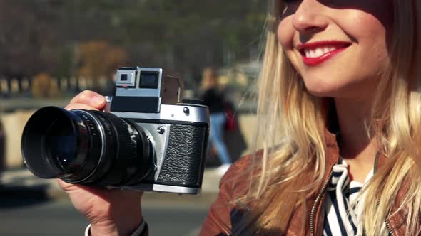 A Young Attractive Woman Takes Photos with a Camera in a Street in an Urban Area - Face Closeup