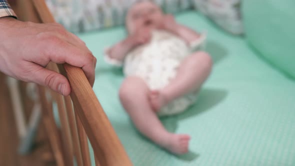 A young dad cradles a newborn baby in a crib.