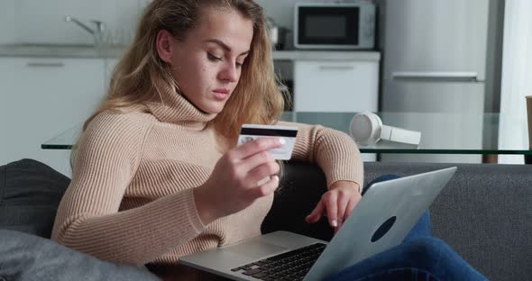 Happy Young Woman with Curly Hair Holding Credit Card Using Laptop Payments at Home