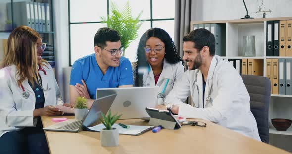 Experienced Multiracial Medical Team in white Coats and Blue Workwear Talking in Clinical Office