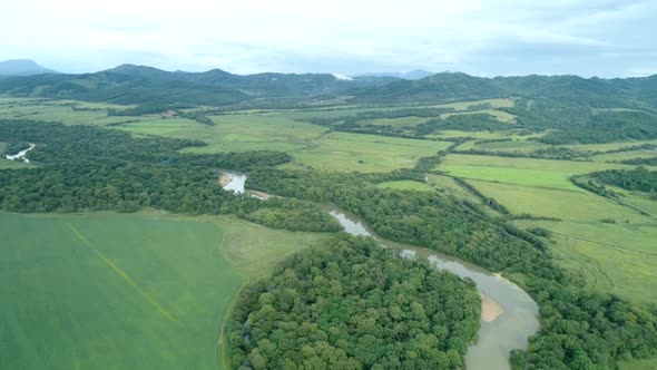 Aerial Drone View Beautiful Natural Scenery of Green Meadow with River Mountains in Background