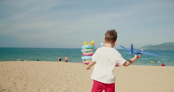 Happy Child Runs with a Toy Plane at Sunset Over the Beach Sand Towards Sea